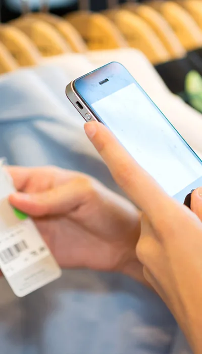 Une cliente relève l’étiquette d’un vêtement sur son téléphone, en magasin